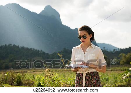 Stock Image - Woman reading book in rural scene, Vang Vieng, Laos. Fotosearch