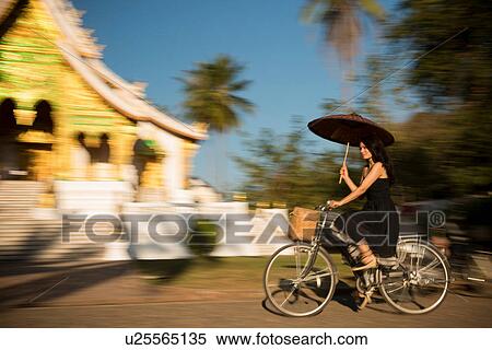 Woman riding bicycle with parasol, Luang Prabang, Laos View Large Photo Image Stock Photography - Woman riding bicycle with parasol, Luang Prabang, Laos. Fotosearch