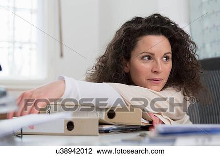 Stock Image - Woman sitting at desk leaning on folders. Fotosearch