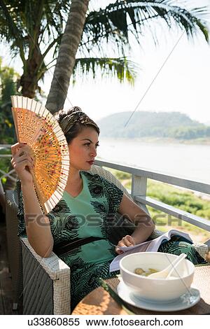 Woman sitting in cafe holding fan View Large Photo Image Stock Photography - Woman sitting in cafe holding fan. Fotosearch