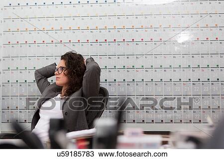 Woman sitting in office chair in front of large wall calendar View Large Photo Image Stock Image - Woman sitting in office chair in front of large wall calendar. Fotosearch