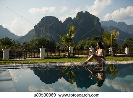 Stock Photo - Woman sitting on poolside, Vang Vieng, Laos. Fotosearch