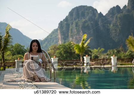Woman sitting reading by swimming pool, Vang Vieng, Laos View Large Photo Image Stock Image - Woman sitting reading by swimming pool, Vang Vieng, Laos. Fotosearch