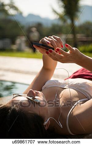 Stock Photo - Woman sunbathing on poolside listening to music. Fotosearch