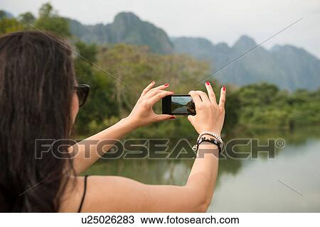 Stock Image - Woman using camera phone, Nam Song River, Vang Vieng, Laos. Fotosearch