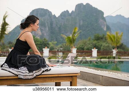 Stock Image - Woman using laptop by poolside, Vang Vieng, Laos. Fotosearch
