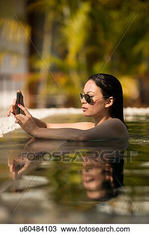 Stock Image - Woman using smartphone in swimming pool. Fotosearch