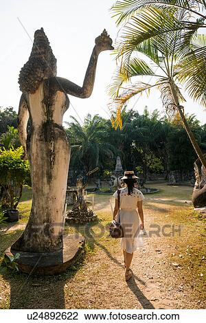 Stock Image - Woman walking past statue, Xieng Khu, Vientiane, Laos. Fotosearch