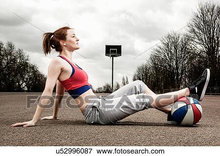 Stock Photo - Woman with ball under one leg sitting on court. Fotosearch