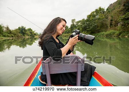 Stock Image - Woman with camera on boat on Nam Song River, Vang Vieng, Laos. Fotosearch