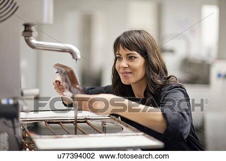 Stock Image - Woman working in commercial kitchen with melted chocolate. Fotosearch