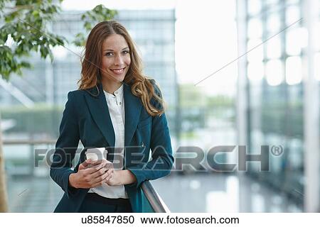 Young business woman within office complex holding coffee View Large Photo Image Stock Image - Young business woman within office complex holding coffee. Fotosearch