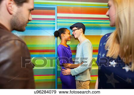 Stock Photo - Young couple embracing, friends in foreground. Fotosearch