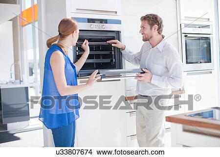 Young couple looking at oven in kitchen showroom View Large Photo Image Picture - Young couple looking at oven in kitchen showroom. Fotosearch