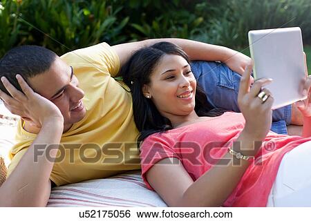 Young couple lying down using digital tablet View Large Photo Image Stock Photograph - Young couple lying down using digital tablet. Fotosearch