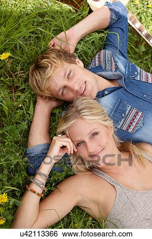 Young couple lying on grass looking at camera View Large Photo Image Stock Photograph - Young couple lying on grass looking at camera. Fotosearch