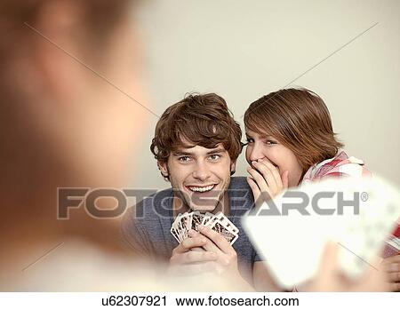 Stock Image - Young couple playing cards and whispering. Fotosearch