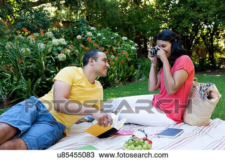 Young couple sitting on picnic blanket, woman photographing man View Large Photo Image Stock Image - Young couple sitting on picnic blanket, woman photographing man. Fotosearch