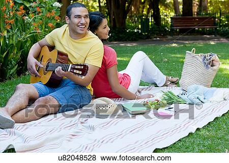 Young couple sitting on picnic blanket, man playing guitar View Large Photo Image Stock Photo - Young couple sitting on picnic blanket, man playing guitar. Fotosearch