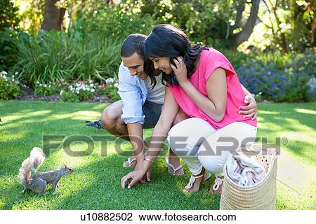 Stock Image - Young couple watching squirrel in garden. Fotosearch