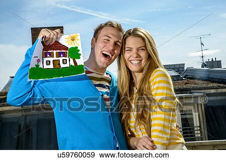 Stock Photo - Young couple with drawing of house on rooftop. Fotosearch