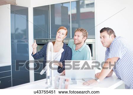 Stock Image - Young couple with salesman in kitchen showroom. Fotosearch