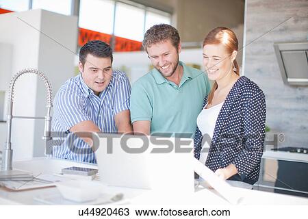 Stock Image - Young couple with salesman in kitchen showroom. Fotosearch