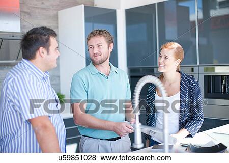 Stock Photo - Young couple with salesman in kitchen showroom. Fotosearch