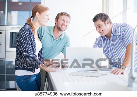 Stock Photograph - Young couple with salesman in kitchen showroom. Fotosearch