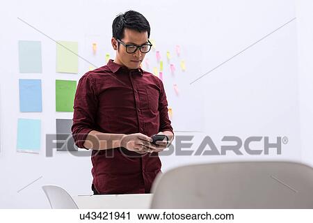 Stock Image - Young male with smartphone in design studio. Fotosearch