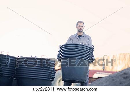 Stock Image - Young man carrying large tubs. Fotosearch