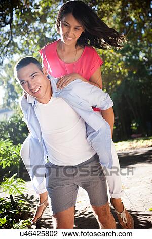Stock Image - Young man giving woman piggy back. Fotosearch