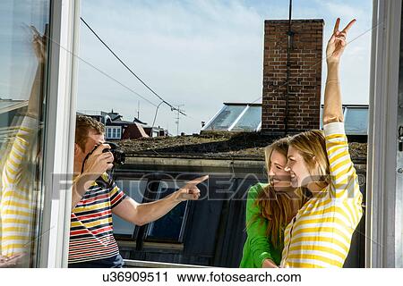 Stock Image - Young man photographing women on rooftop. Fotosearch