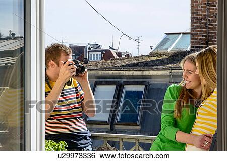 Stock Photograph - Young man photographing women on rooftop. Fotosearch