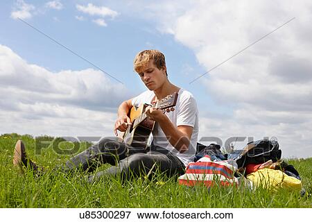 Young man playing guitar on grass View Large Photo Image Stock Photo - Young man playing guitar on grass. Fotosearch