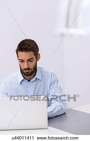 Stock Image - Young man sitting behind laptop in office. Fotosearch