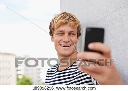 Stock Photograph - Young man taking self portrait on smartphone. Fotosearch