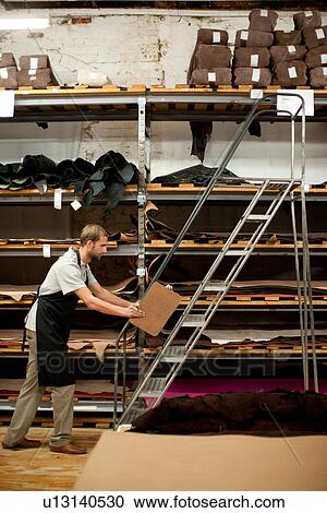 Stock Image - Young man working in leather stockroom. Fotosearch