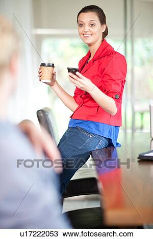 Stock Image - Young woman in office with cell phone and coffee. Fotosearch