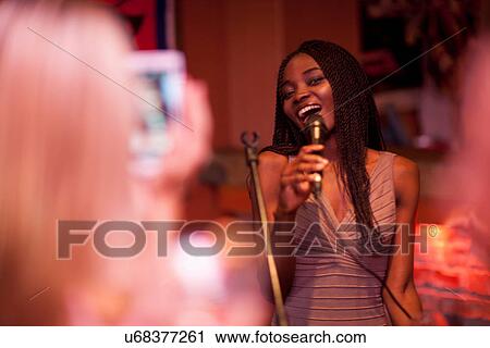 Stock Image - Young woman singing with microphone. Fotosearch