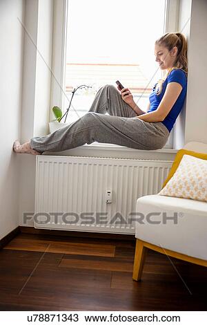 Young woman sitting on windowsill using cell phone View Large Photo Image Stock Image - Young woman sitting on windowsill using cell phone. Fotosearch