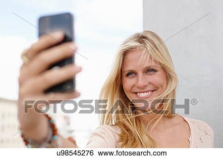 Stock Photograph - Young woman taking self portrait on smartphone. Fotosearch
