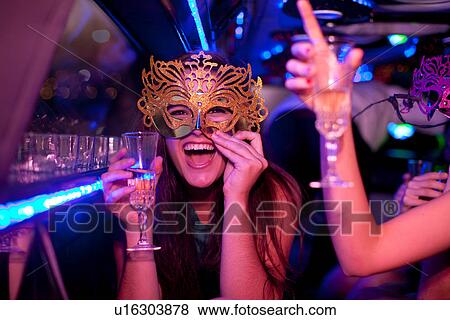 Stock Photo - Young woman wearing mask with wine glass in limousine. Fotosearch