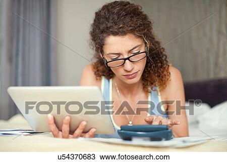 Stock Image - Young woman with calculator and digital tablet. Fotosearch