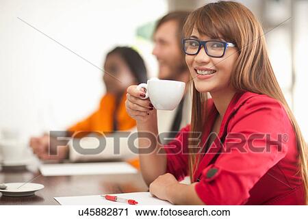 Young woman with coffee smiling towards camera View Large Photo Image Stock Image - Young woman with coffee smiling towards camera. Fotosearch