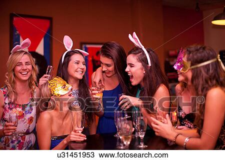 Stock Image - Young women laughing with drinks at hen party. Fotosearch