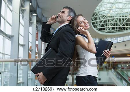 Stock Photo - Businessman and Businesswoman back to back on mobile phones. Fotosearch