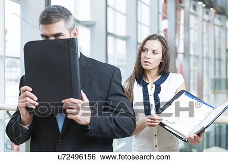 Businessman hides from coworker behind folder View Large Photo Image Stock Photograph - Businessman hides from coworker behind folder. Fotosearch