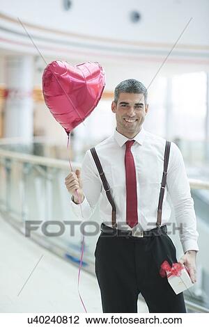 Businessman holding heart shaped balloon and present View Large Photo Image Stock Image - Businessman holding heart shaped balloon and present. Fotosearch