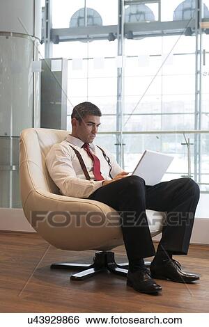 Stock Photograph - Businessman in arm chair working on laptop. Fotosearch